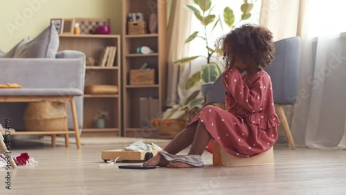 Cute African American girl in polka dot dress on potty in living room