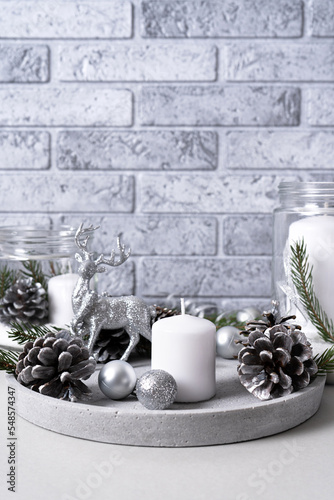 Stone plate with candles, fir branches and pine cones with silver Christmas decorations.