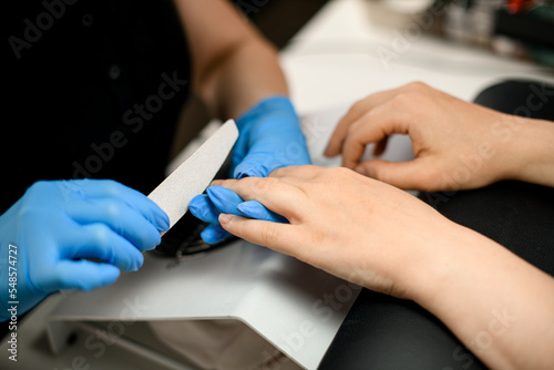 Close-up of hands of skilled manicurist filing female nails with nail file