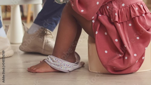 Cropped shot of unrecognizable toddler girl in pretty polka dot dress on potty at home