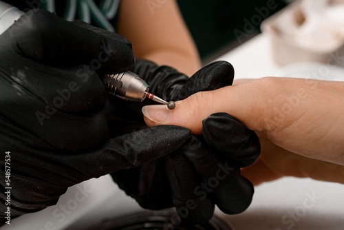 Close-up of hands of manicurist in gloves removing cuticle on woman hand with professional electric nail drill