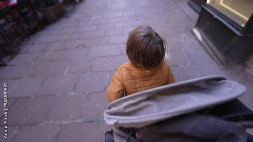 One child sitting in a stroller strolling in European street. 2 year old small boy seated. mother perspective One child sitting in a stroller strolling in European street. 2 year old small boy seated. mother perspective