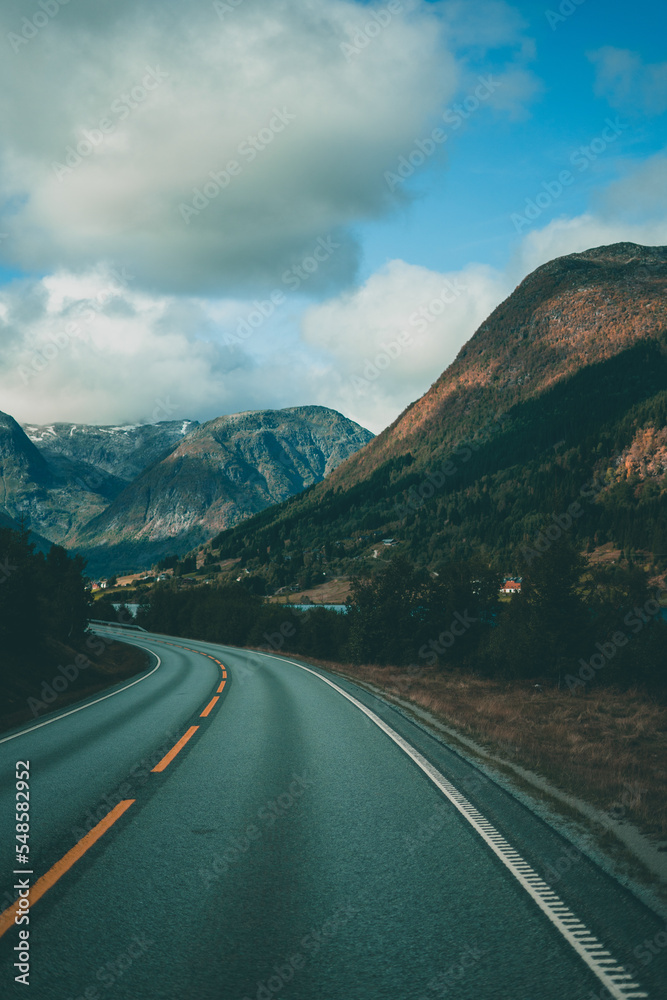 Empty road leading to the mountains on a moody day in Norway with clouds Empty road leading to the mountains on a moody day in Norway with clouds