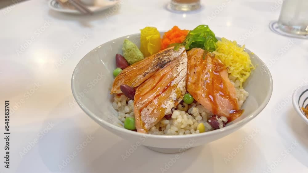 Delicious Japanese food salmon don with whole grain rice. Bowl with fish grill and Rice. Healthy Food. Luxury Appetizer in Restaurant. female hand pouring soy sauce or shoyu on rice Delicious Japanese food salmon don with whole grain rice. Bowl with fish grill and Rice. Healthy Food. Luxury Appetizer in Restaurant. female hand pouring soy sauce or shoyu on rice