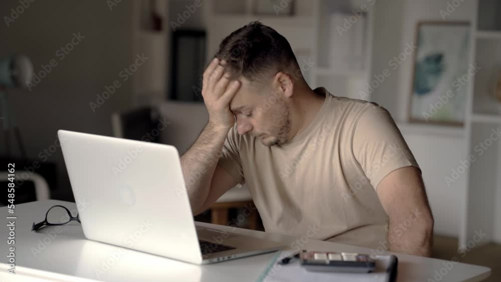Male hipster freelance businessman tired working at laptop computer, has pain in head taking off glasses and touching eyes. Exhausted working at screen has eye strain, dry eyes and need eye drops Male hipster freelance businessman tired working at laptop computer, has pain in head taking off glasses and touching eyes. Exhausted working at screen has eye strain, dry eyes and need eye drops