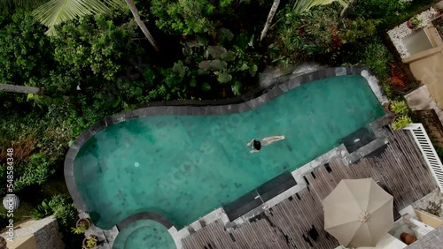 Aerial view woman jumping and dives into the pool and swims under the water at tropical hotel spa with view of jungle luxury hotel lifestyle while vacation