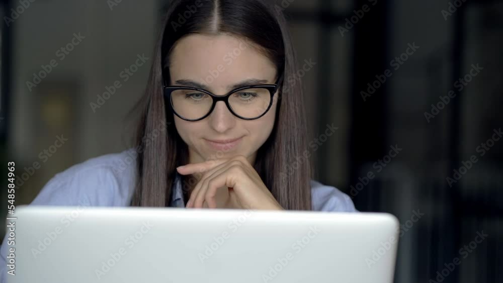 Closeup view of pretty young woman with blue eyes in glasses watching the screen of laptop checking results of work. Freelance manager working from home happy smiling and nodding Closeup view of pretty young woman with blue eyes in glasses watching the screen of laptop checking results of work. Freelance manager working from home happy smiling and nodding
