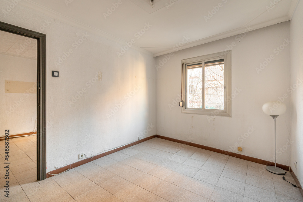 Empty spacious room with window and dirty walls in an old flat before renovation.