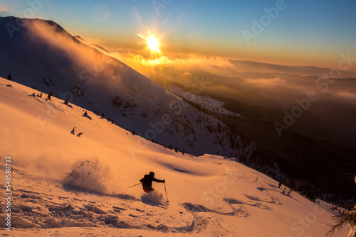 Freeride skier in a beautiful snowy mountains covered with a sunset orange cloudy sky. Adrenaline outdoor winter adventures © almostfuture