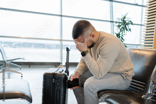Sad man waiting for delayed flight in airport. Young guy worrying something, sitting and touch his head at the airport terminal. Businessman miss his flight. 