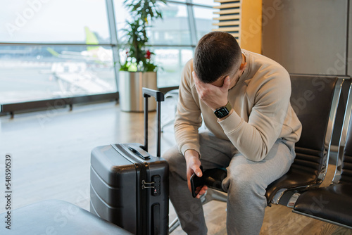 Sad man waiting for delayed flight in airport. Young guy worrying something, sitting and touch his head at the airport terminal. Businessman miss his flight. 