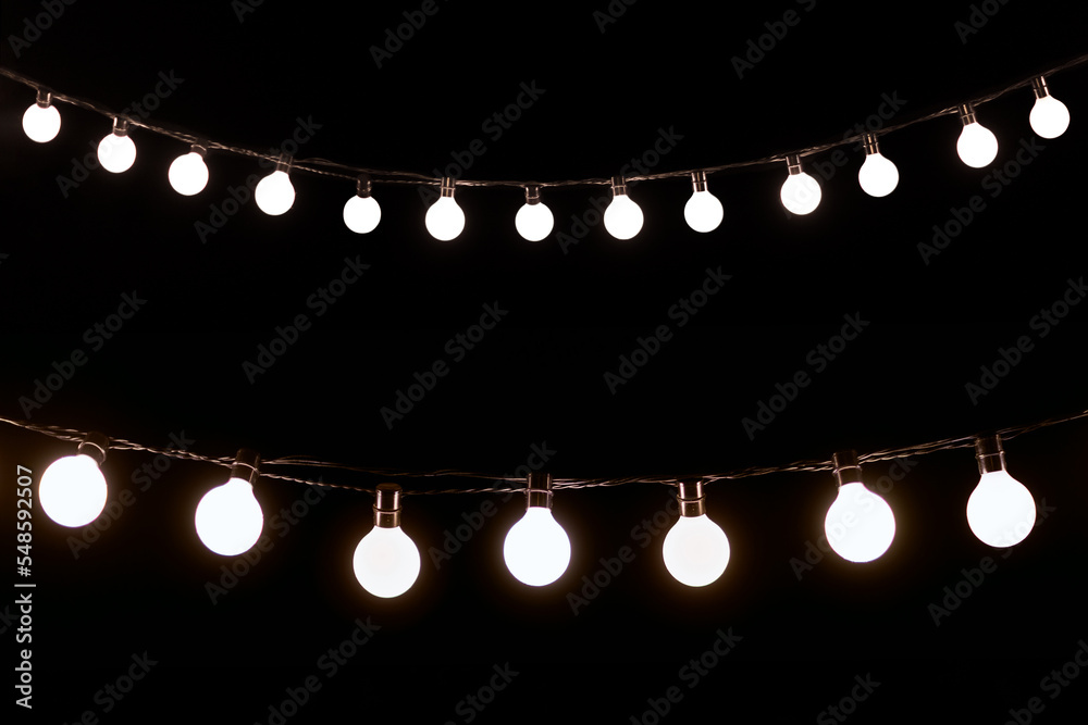 Blurred glowing light bulb garland, electric garland on black background, mock-up for design, cold light