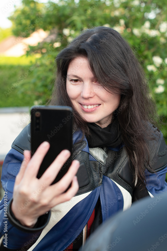 Fototapeta premium young beautiful brunette biker chatting with friends on a mobile phone