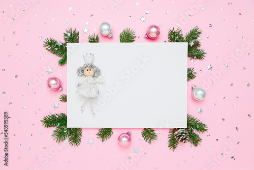 Christmas card with copy space. Princess on blank white paper in frame of natural fir tree branches and decorations on pastel pink flat lay background. photo