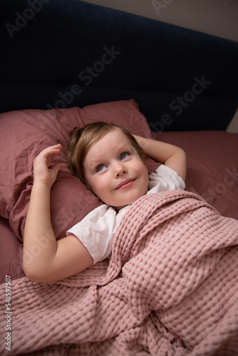 A little boy lies in bed on pink underwear in a white T-shirt and dreams of throwing his hands back.