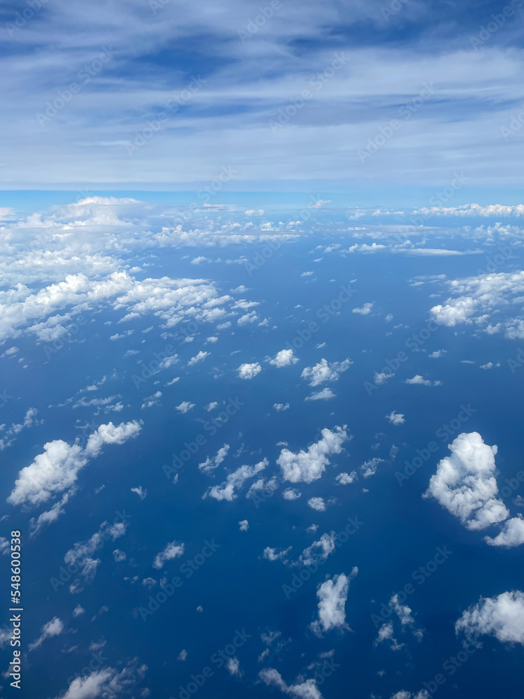 Fototapeta premium Stunning view of the expanse of land and sky, shot from thousand feet above the ground among white clouds. Smartphone photography