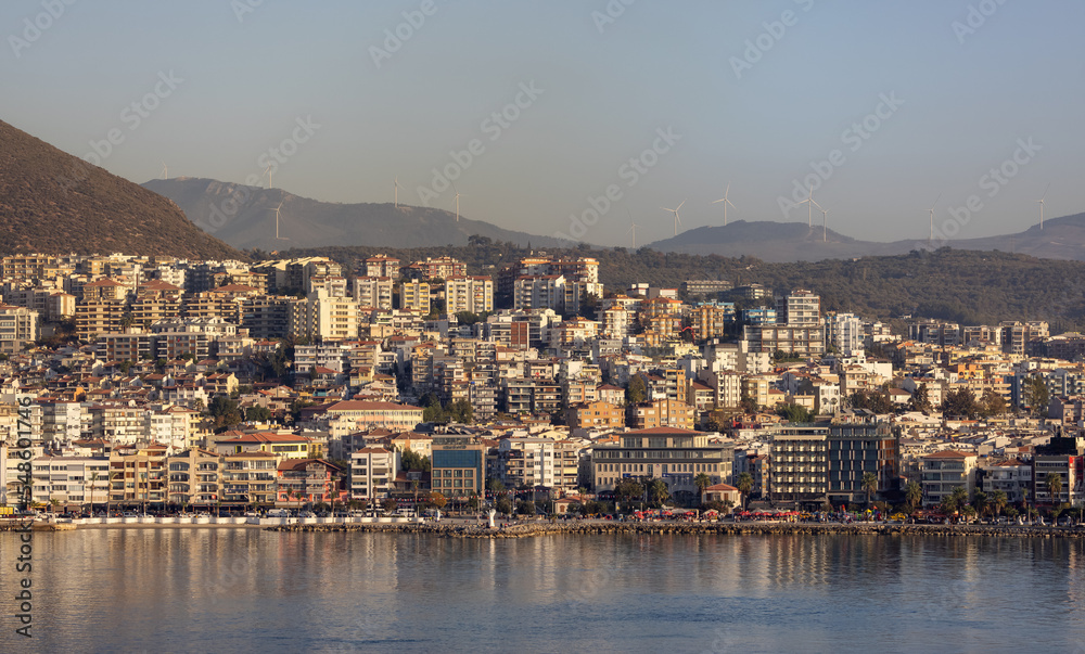 Homes and Buildings in a Touristic Town by the Aegean Sea. Kusadasi, Turkey. Sunny Evening. Mountain with Wind Turbine.