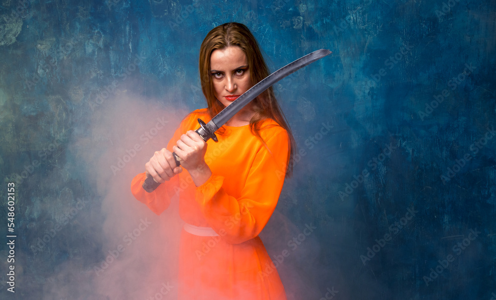 Portrait of a beautiful woman in an orange dress and with a samurai sword in her hands. Strength and beauty - concept.