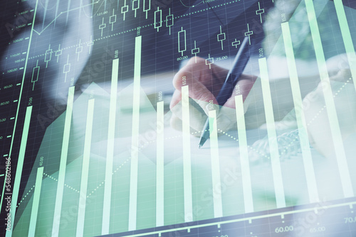 Financial forex graph displayed on hands taking notes background. Concept of research. Multi exposure