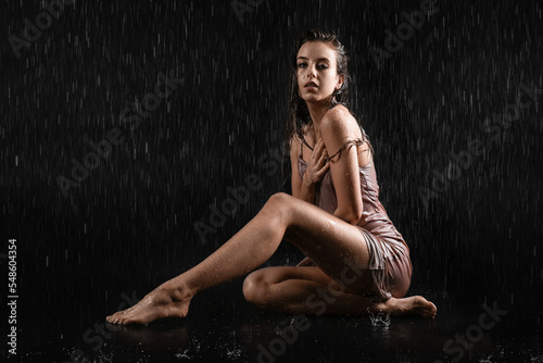 Attractive young woman with dripping water sitting on black background