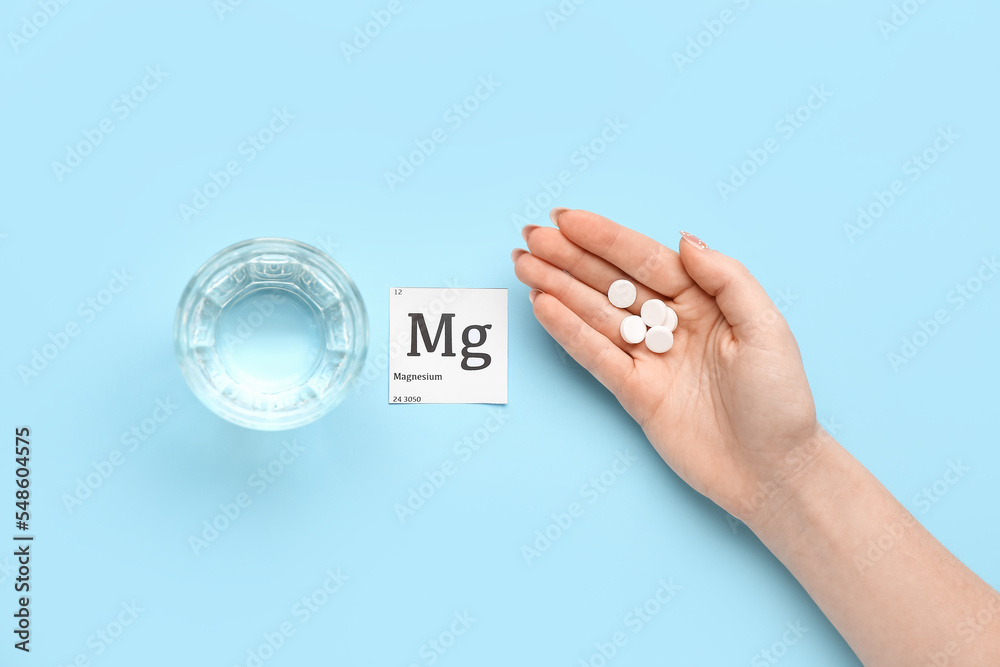 Female hand with magnesium pills and glass of water on blue background - obrazy, fototapety, plakaty 