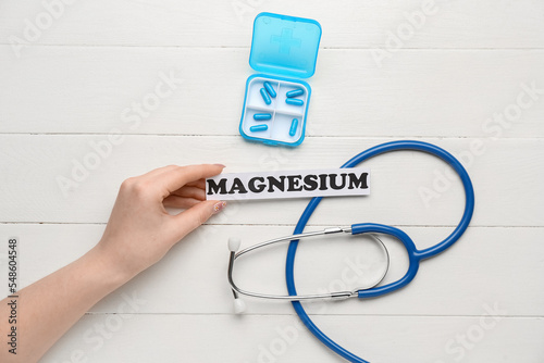 Female hand with word MAGNESIUM, pills and stethoscope on light wooden background