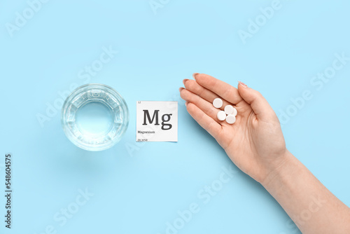Photos Female hand with magnesium pills and glass of water on blue background