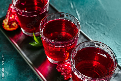 Board with glasses of fresh pomegranate juice on dark color background, closeup