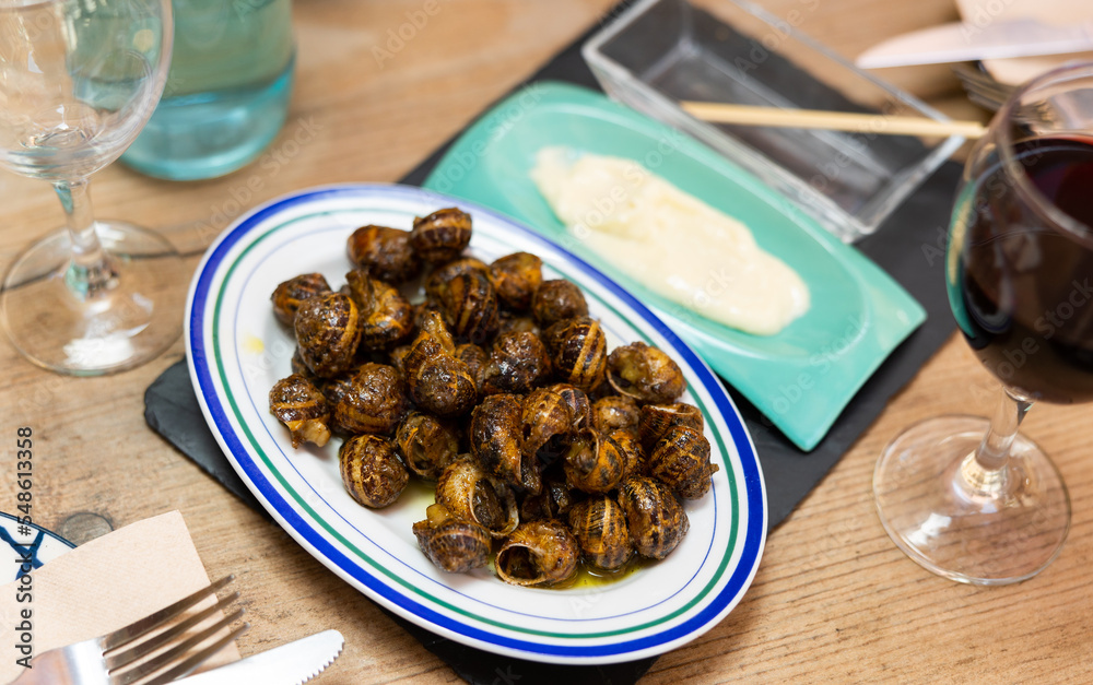Plate of Caracoles a la llauna, delicacy of Catalan cuisine of land snails cooked in shells on grill accompanied by aioli sauce. Authentic cuisine