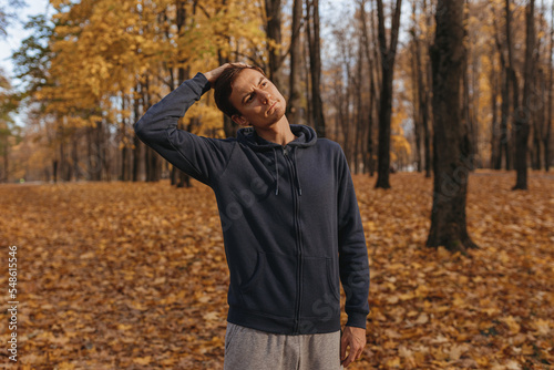 Sporty male runner stretching and warming up neck and head while preparing for training in autumn park  © Dzmitry