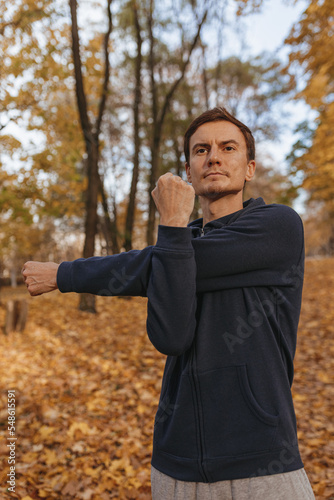 Athletic man in sportswear stretching arms and exercising during fitness training in autumn park 