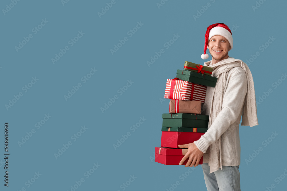 Handsome man in Santa hat with Christmas presents on blue background Handsome man in Santa hat with Christmas presents on blue background