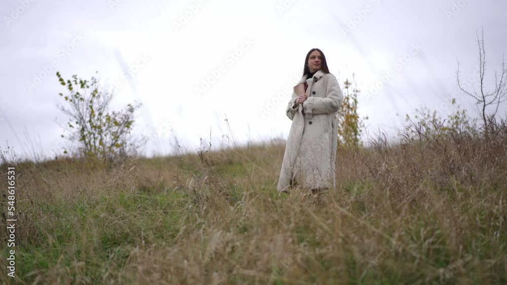 Wide shot beautiful young woman walking in slow motion on autumn meadow looking around. Portrait of confident Caucasian brunette lady strolling outdoors leaving. Solitude and lifestyle Wide shot beautiful young woman walking in slow motion on autumn meadow looking around. Portrait of confident Caucasian brunette lady strolling outdoors leaving. Solitude and lifestyle