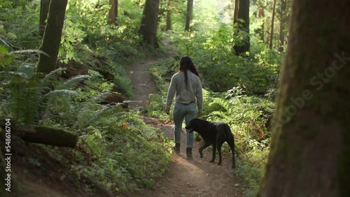 Young attractive female walking in beautiful forest with her dog