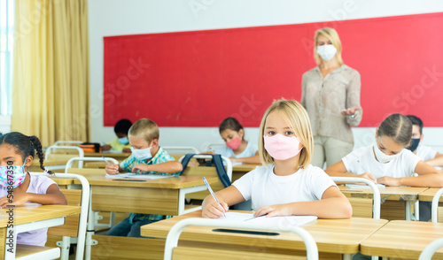 Diligent tween girl in protective mask studying in school with classmates. New life reality in coronavirus pandemic