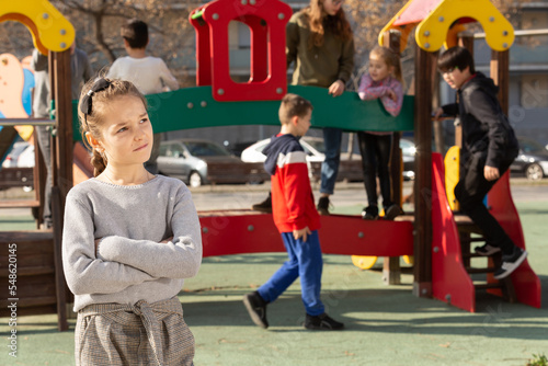 Portrait of offended girl not playing with friends after quarrel on playground. High quality photo