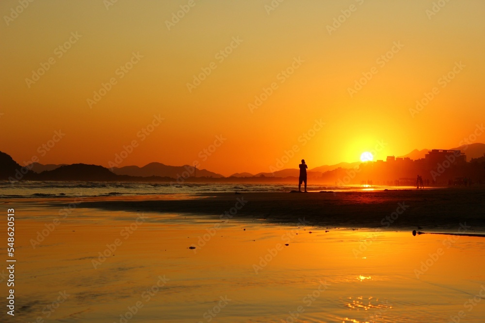 Man in silhouette standing alone on the beach sand during sunset. Riviera Beach, Bertioga, Brazil. reddish sky