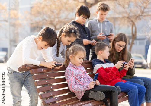 Group of children playing with smartphones outdoors at sunny spring day © JackF