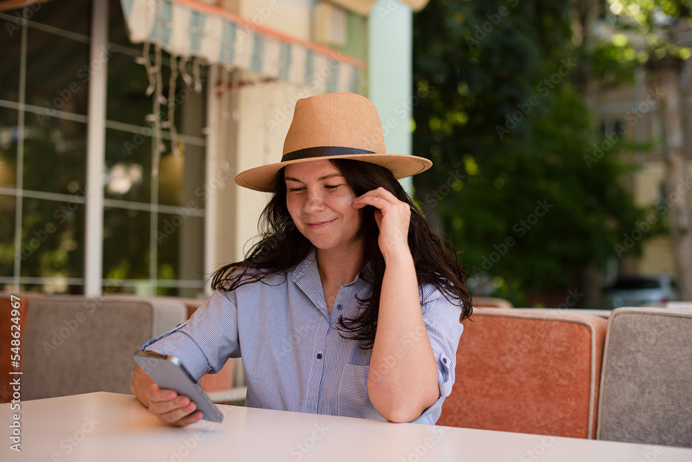 Stylish woman in hat with smartphone outside.