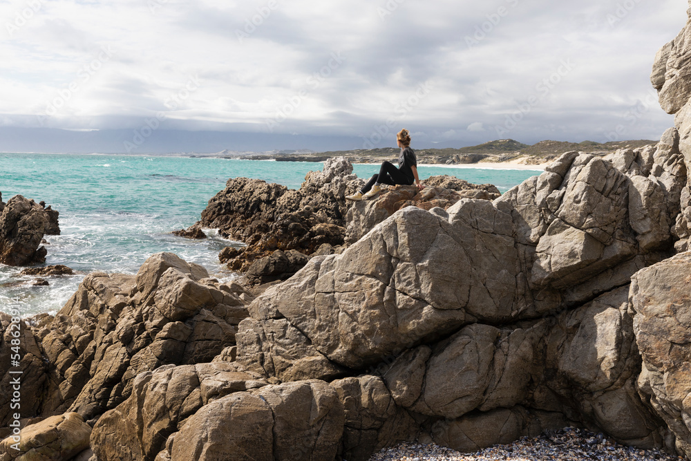 South Africa, Gansbaai, Teenage girl (16-17) sitting on rocks on sea coast South Africa, Gansbaai, Teenage girl (16-17) sitting on rocks on sea coast