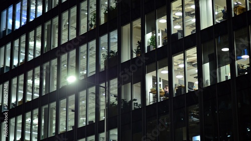 Modern office building in city at the night. View on illuminated offices of a corporate building. Blinking light in window of the multi-storey building of glass and steel. Long exposure at night