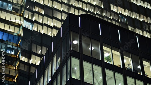 Modern office building in city at the night. View on illuminated offices of a corporate building. Blinking light in window of the multi-storey building of glass and steel. Long exposure at night