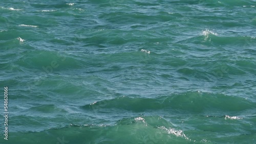 Panning up shot of rough waves on Lake Michigan with greenish blue or turquoise water as sun lights up the splashing  and sloshing water.
