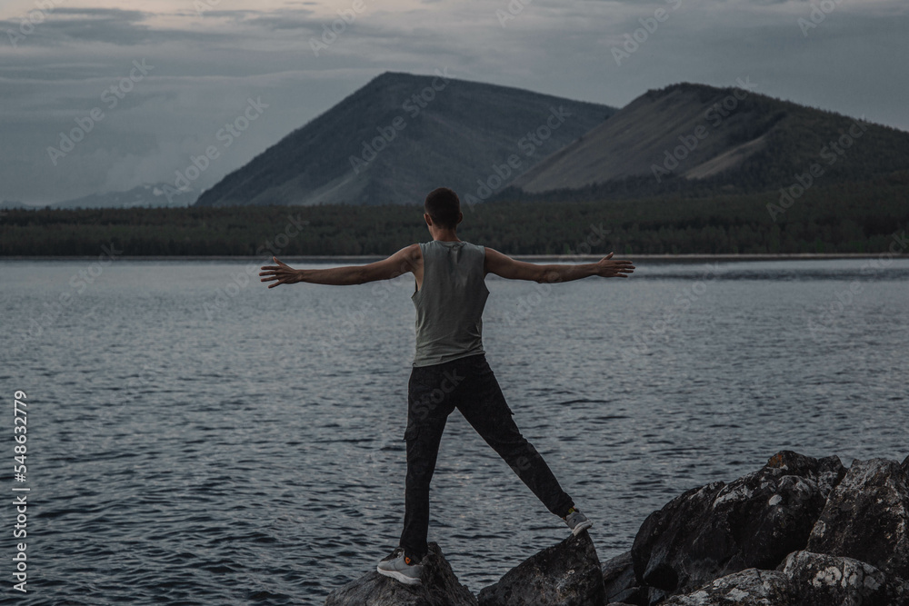 a young man with his arms outstretched stands on the shore of the lake a young man with his arms outstretched stands on the shore of the lake