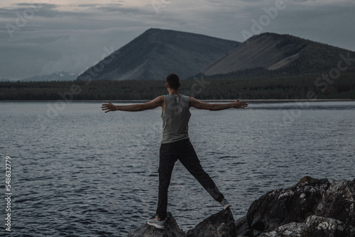 a young man with his arms outstretched stands on the shore of the lake