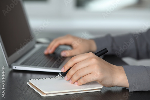 Woman with pen, laptop and notebook at wooden table, closeup. Electronic document management © New Africa