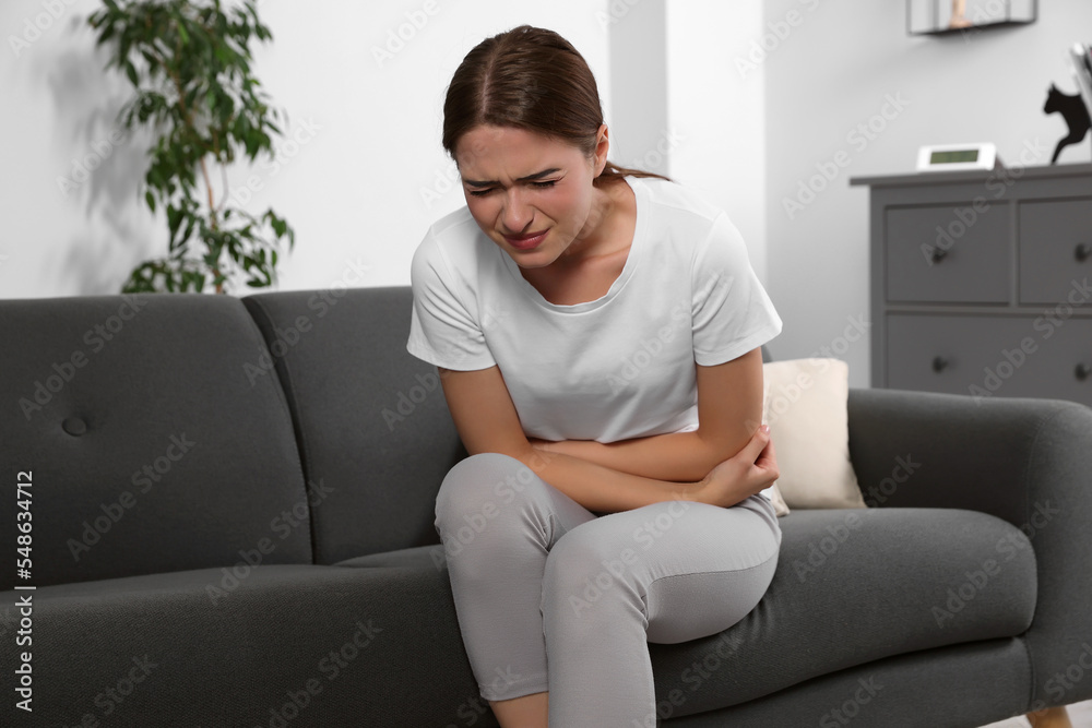 Young woman suffering from cystitis on sofa at home