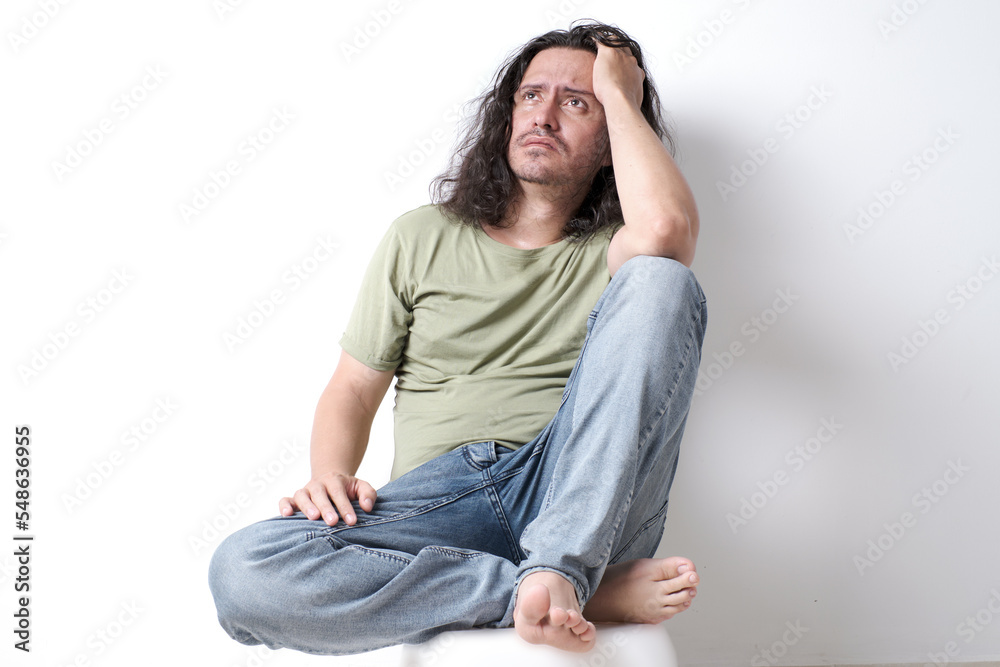 latin man sitting pensively with his hand on his head looking upwards latin man sitting pensively with his hand on his head looking upwards