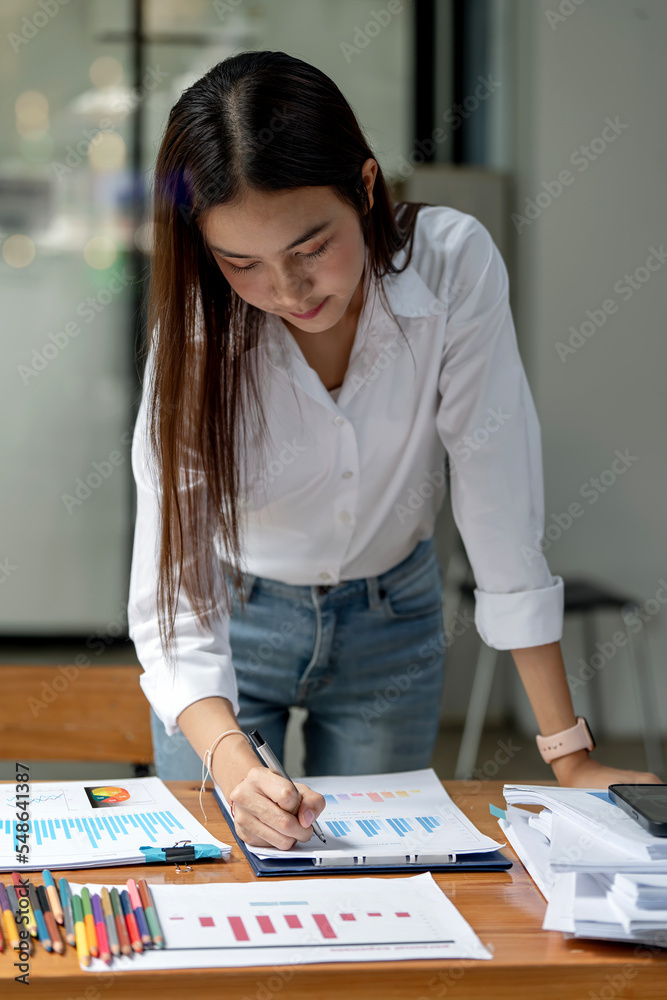 Fototapeta premium Young business woman working on paperwork and statistics graphs.