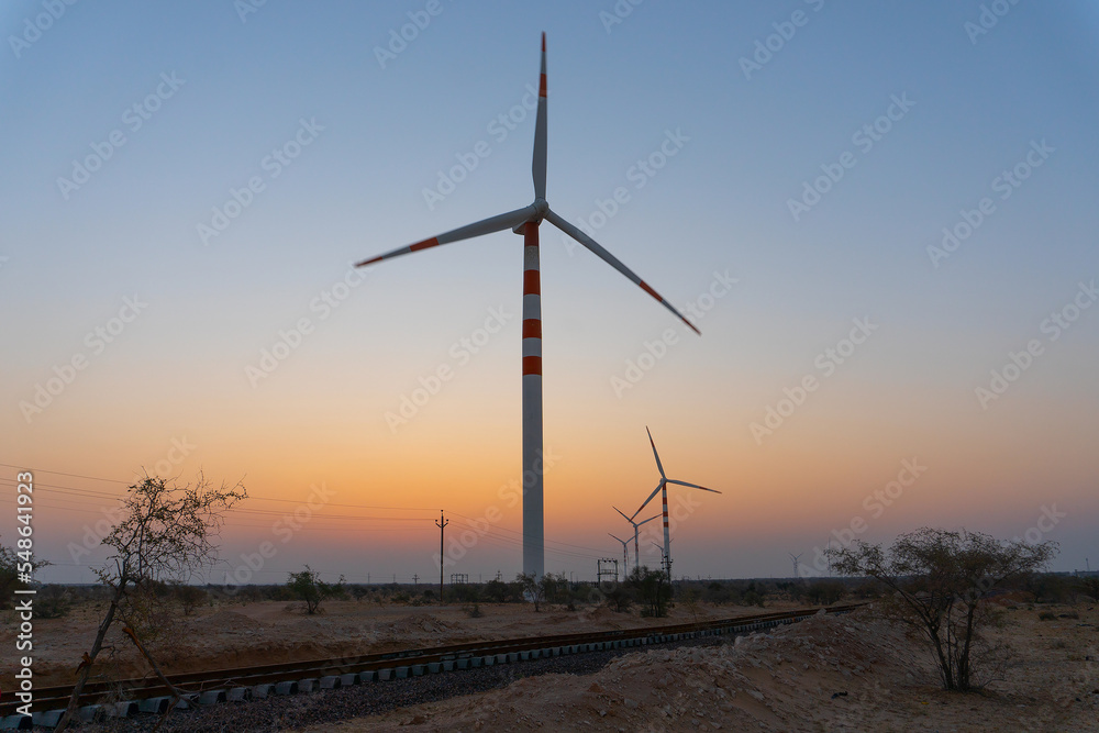 Obraz premium Pre dawn light in desert sky with Electrical power generating wind mills producing alterative eco friendly green energy for consumption by local people. Thar desert, Rajasthan, India.
